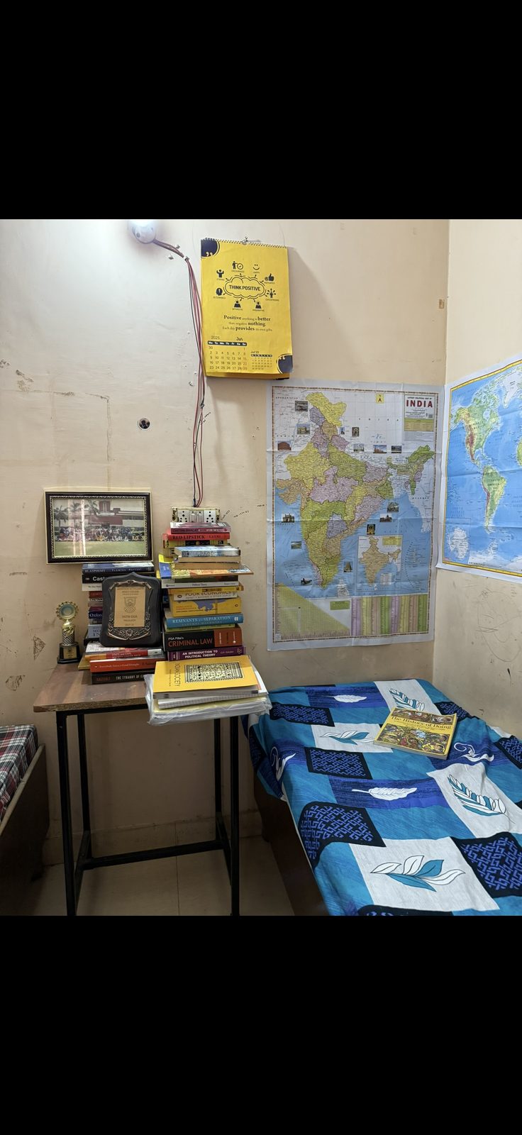 A lived-in room with a desk, books, maps, and a framed photograph